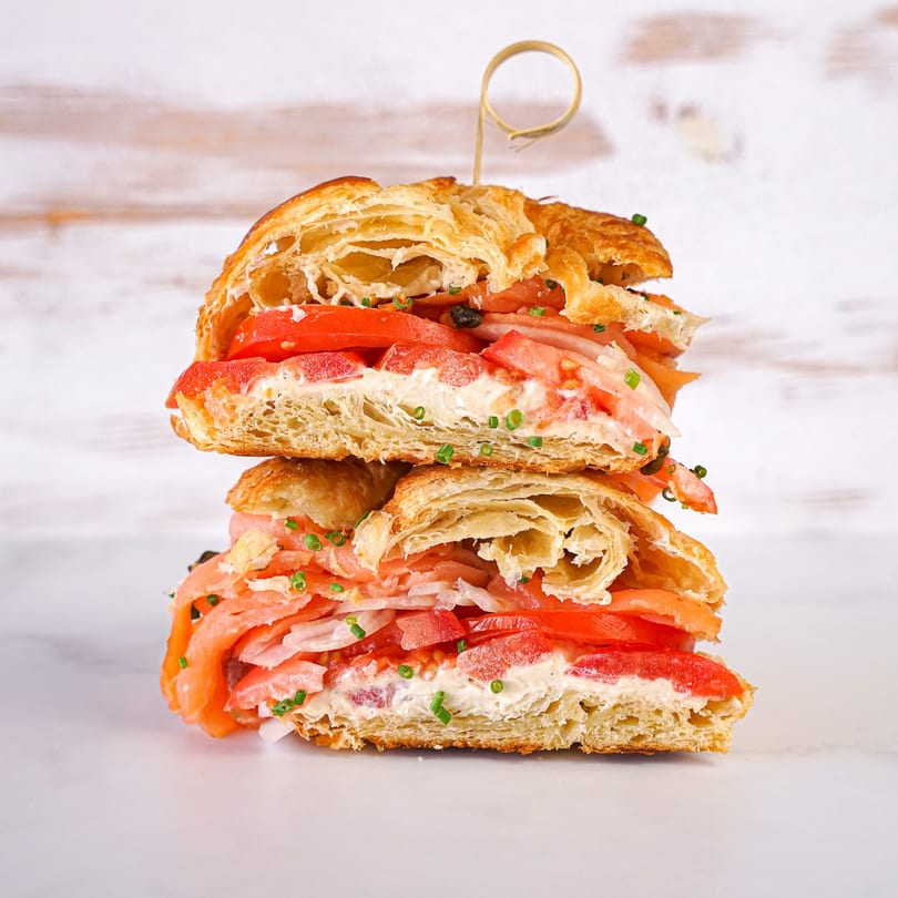 Two halves of a croissant sandwich with salmon, cream cheese, tomatoes, and chives, stacked.