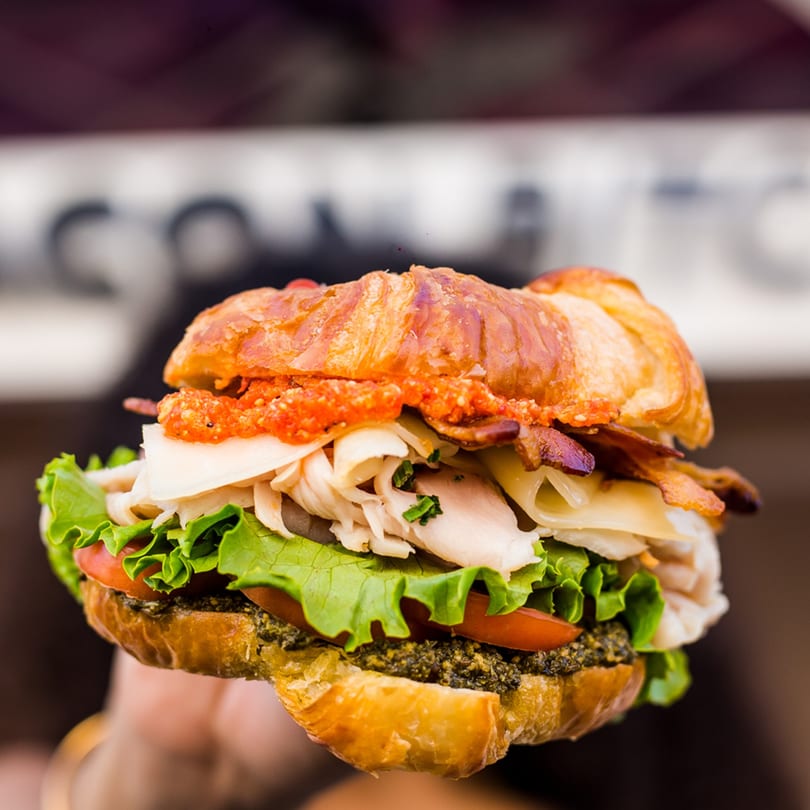 A Bacon Bitch croissant sandwich with bacon, turkey, cheese, lettuce, tomato, and pesto.