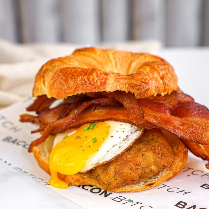 A Bacon Bitch breakfast sandwich with bacon, fried egg, and chicken on a croissant.