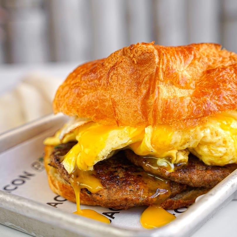 A Bacon Bitch breakfast sandwich with sausage, egg, and melted cheese on a croissant.